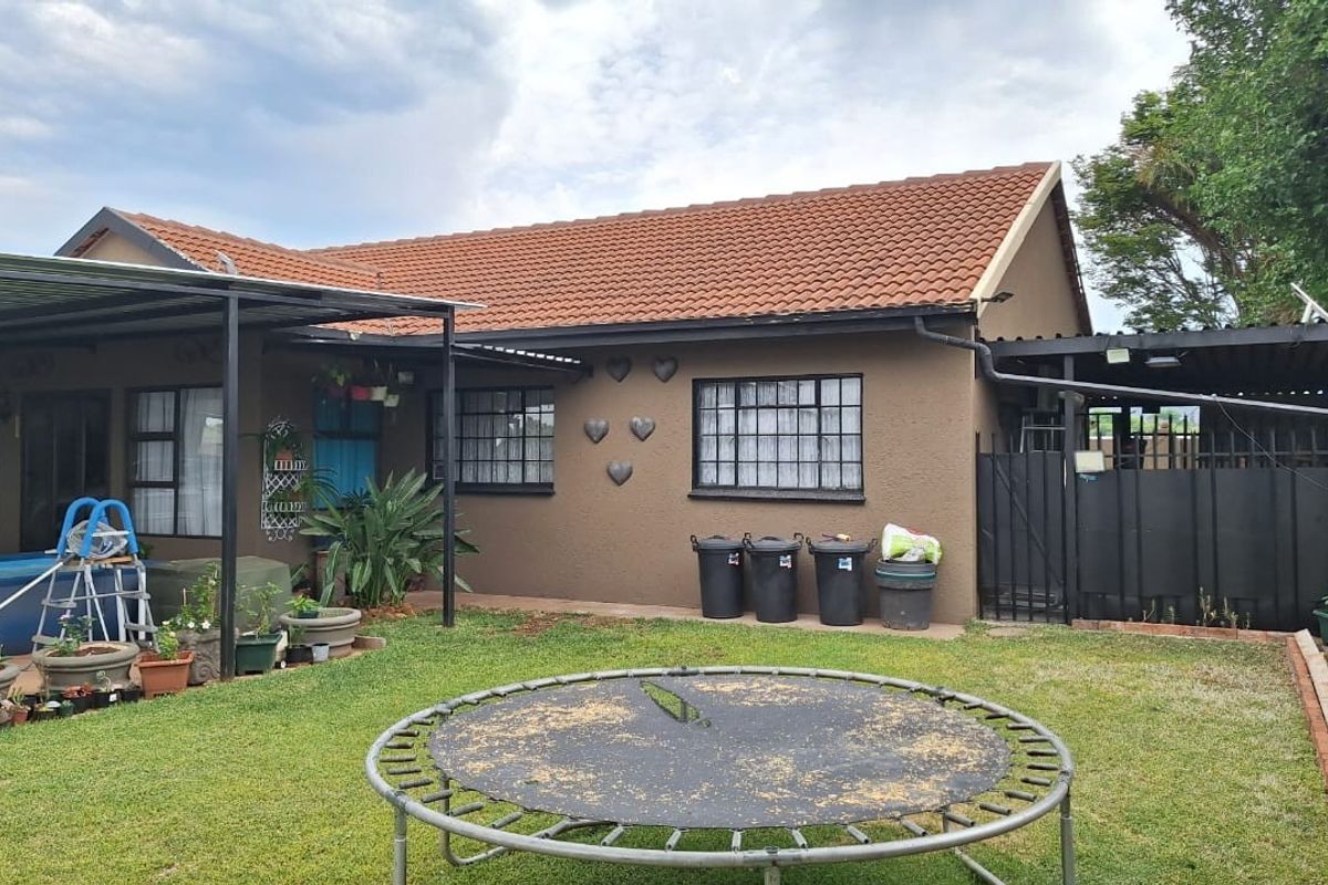 Rear view of the townhouse featuring a tiled roof, covered patio area, and a private garden space with perimeter fencing.