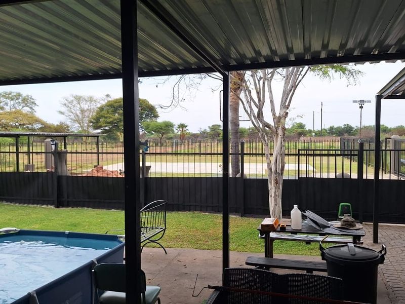 Covered outdoor patio area featuring a metal roof structure, paved flooring, and direct access to the garden and fenced perimeter.