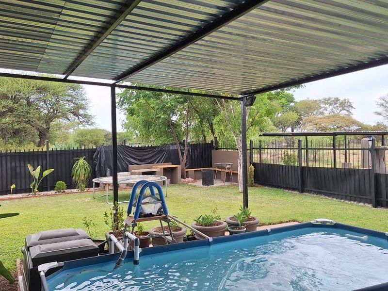 Outdoor entertainment area featuring a covered patio, built-in braai, and a swimming pool set within a fenced garden.
