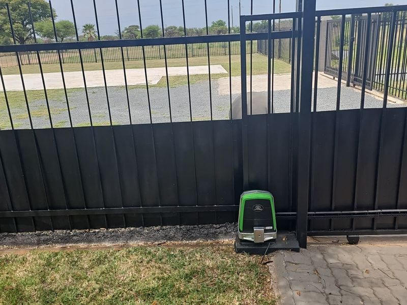 A secure sliding gate featuring an automated electric motor, providing access to a paved driveway and fenced property perimeter.