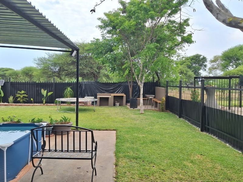 Rear garden area featuring a covered patio, built-in braai, concrete flooring, and perimeter metal fencing.