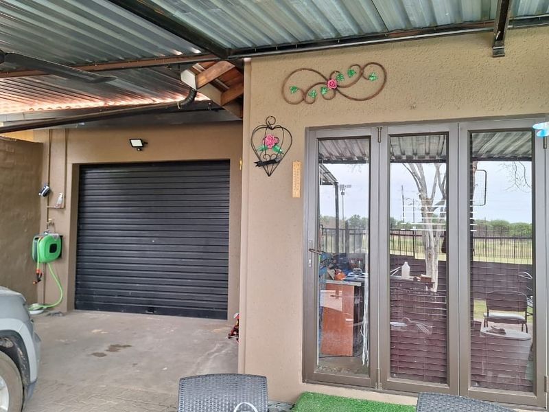 A covered patio area featuring a corrugated metal roof, ceiling fan, and direct access to the garage and interior living space via glass doors.