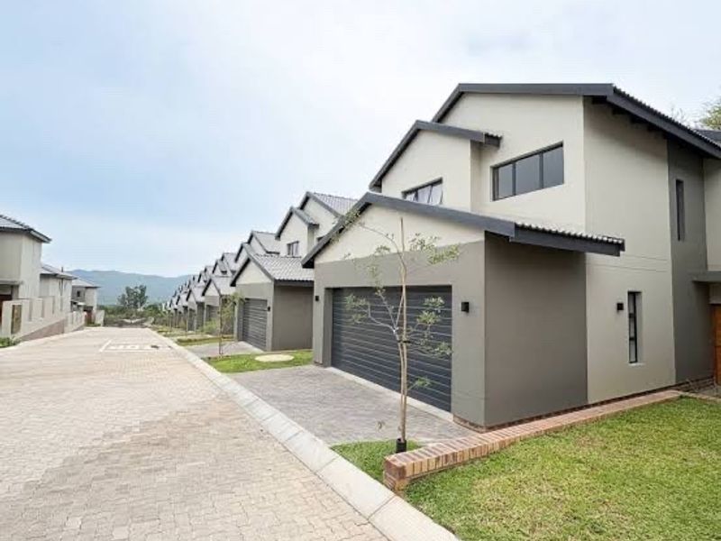 Modern townhouse exterior featuring a paved driveway, double garage, and well-maintained lawn in a contemporary residential estate.