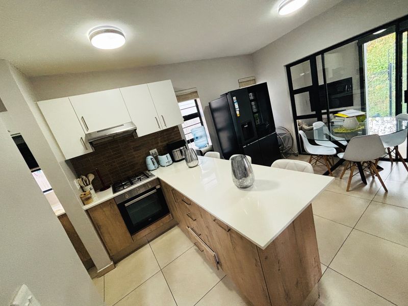 Modern open-plan kitchen featuring a central island with quartz countertops, built-in oven, gas hob, and sleek cabinetry, seamlessly flowing into the dining area.