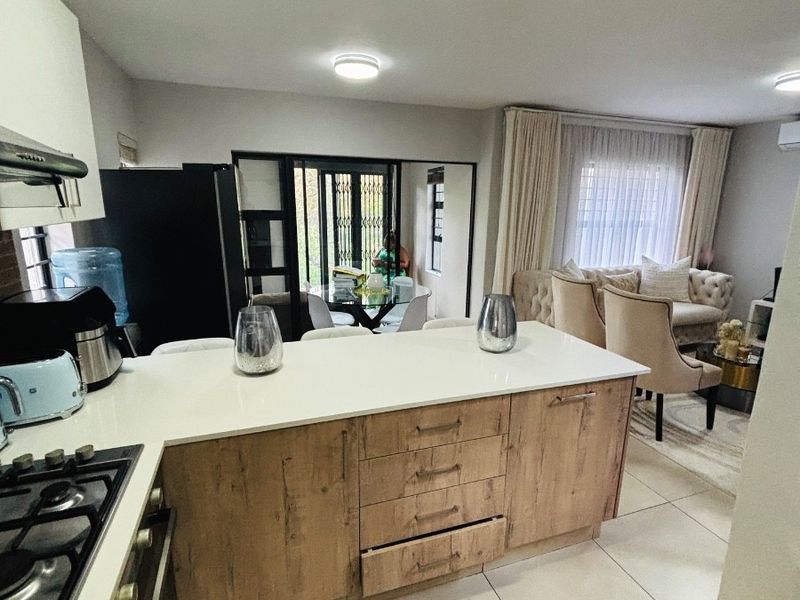 Open-plan kitchen and living area featuring a central island with gas hob, modern cabinetry, and tiled flooring, flowing into a bright lounge space.