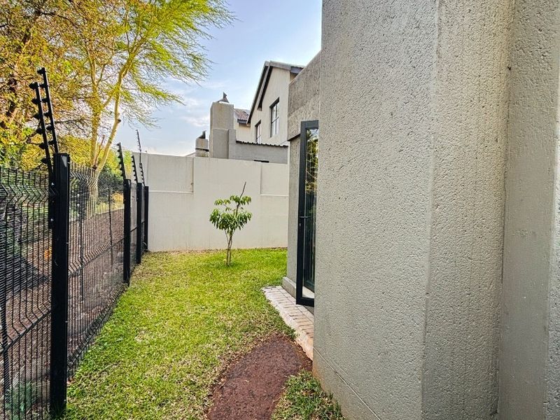 A side garden area featuring a paved pathway, lawn, and secure perimeter fencing with integrated electric security wires.