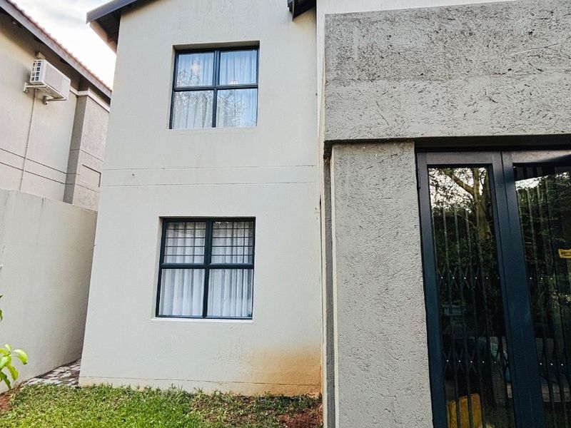 Rear elevation of a two-story townhouse featuring plastered walls, aluminium window frames with security bars, and a sliding security gate.