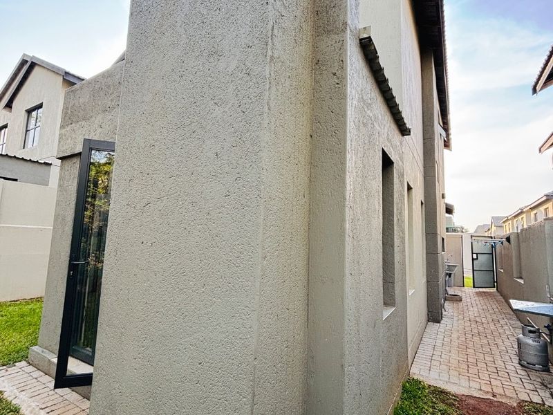 Side view of the townhouse exterior featuring a textured plaster facade, paved walkway, and access to the rear garden area.