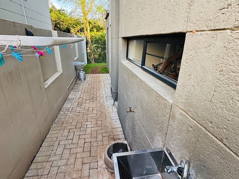 A paved side utility area featuring a stainless steel sink, external water tap, and boundary wall access.