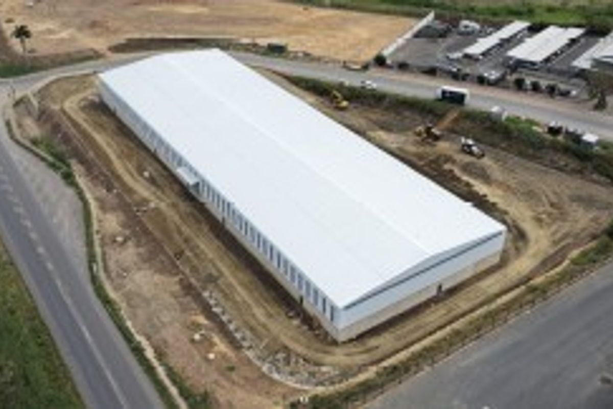 Aerial view of a large industrial warehouse building situated on a corner plot with surrounding access roads and undeveloped grounds.