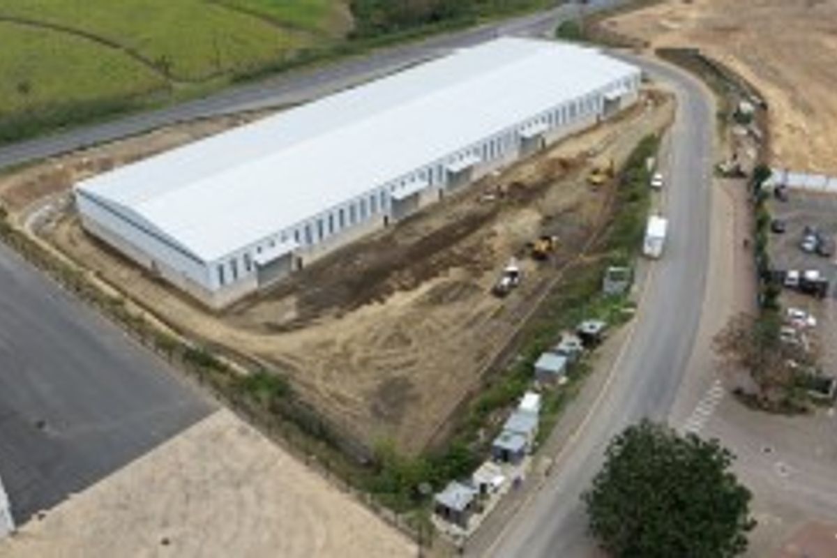Aerial view of a large industrial warehouse facility under development, featuring a metal roof, paved access roads, and surrounding undeveloped land.