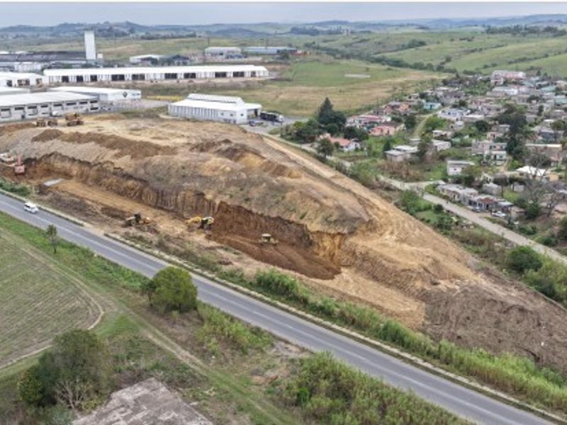 Aerial view of an industrial development site showing ongoing earthworks and excavation near a main road and surrounding residential area.