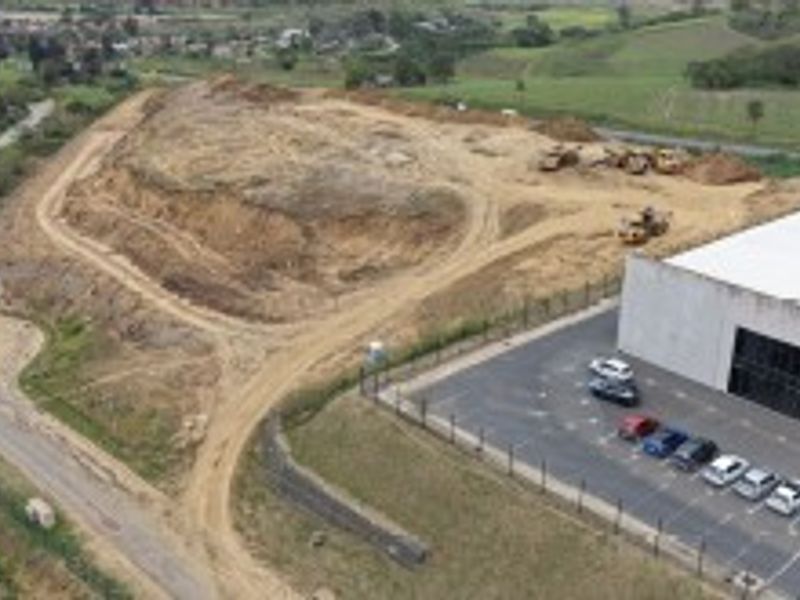 Aerial view of an industrial property featuring a warehouse building, paved parking area, and adjacent undeveloped land with access roads.
