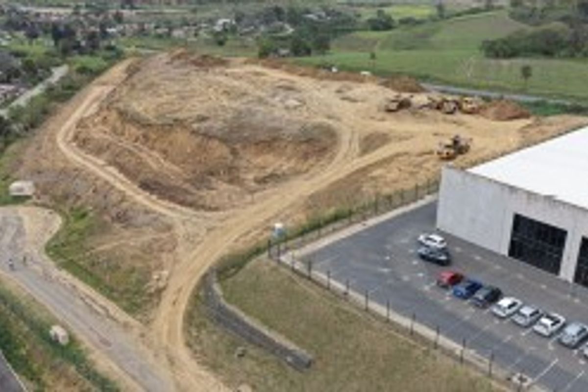 Aerial view of an industrial property featuring a warehouse building, paved parking area, and adjacent undeveloped land with access roads.