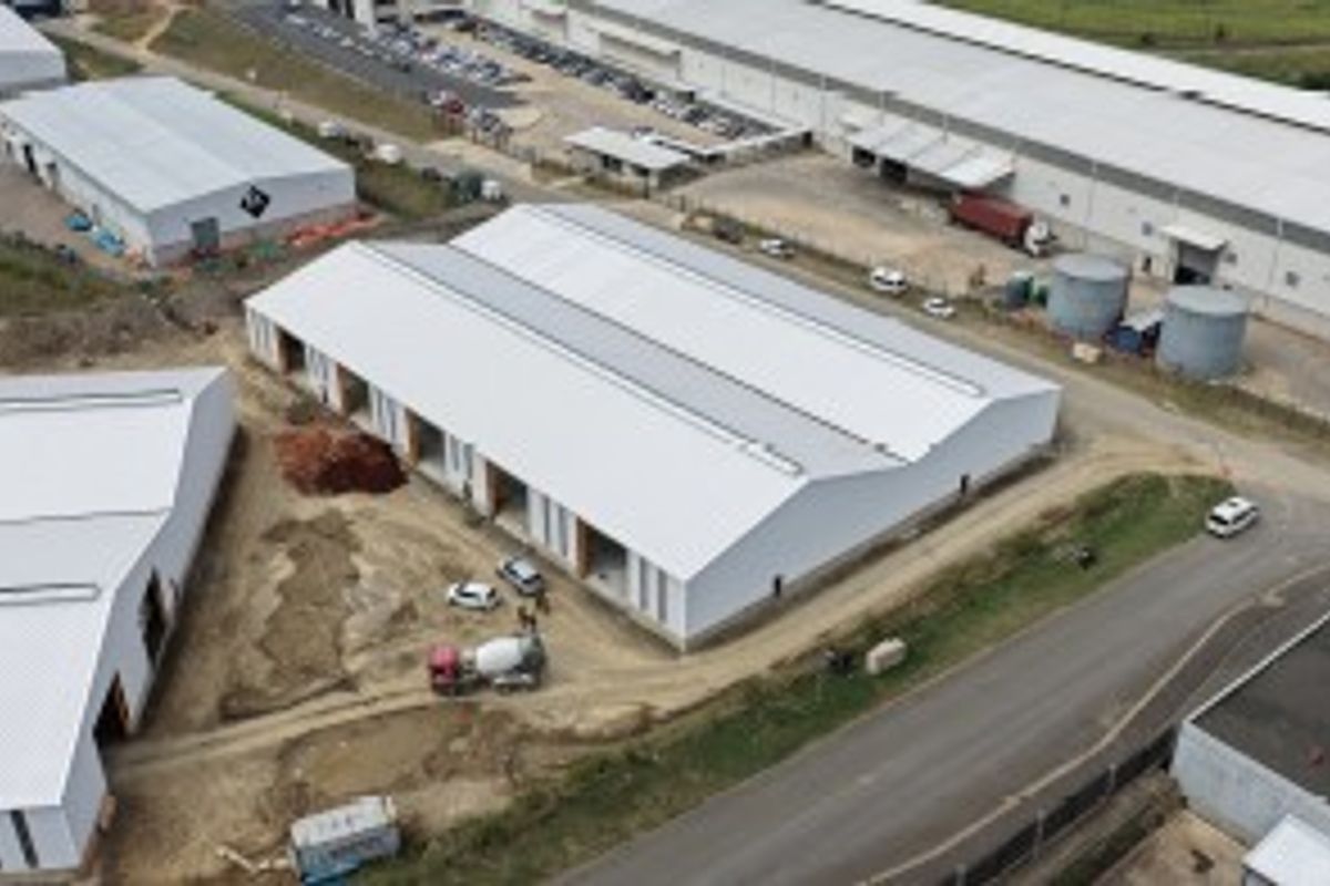 Aerial view of an industrial warehouse complex under development, featuring metal roofing and surrounding site access roads.
