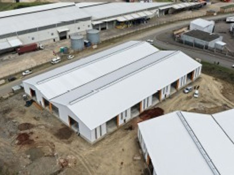 Aerial view of an industrial warehouse complex featuring a large metal roof, multiple roller shutter door openings, and surrounding unpaved yard space.