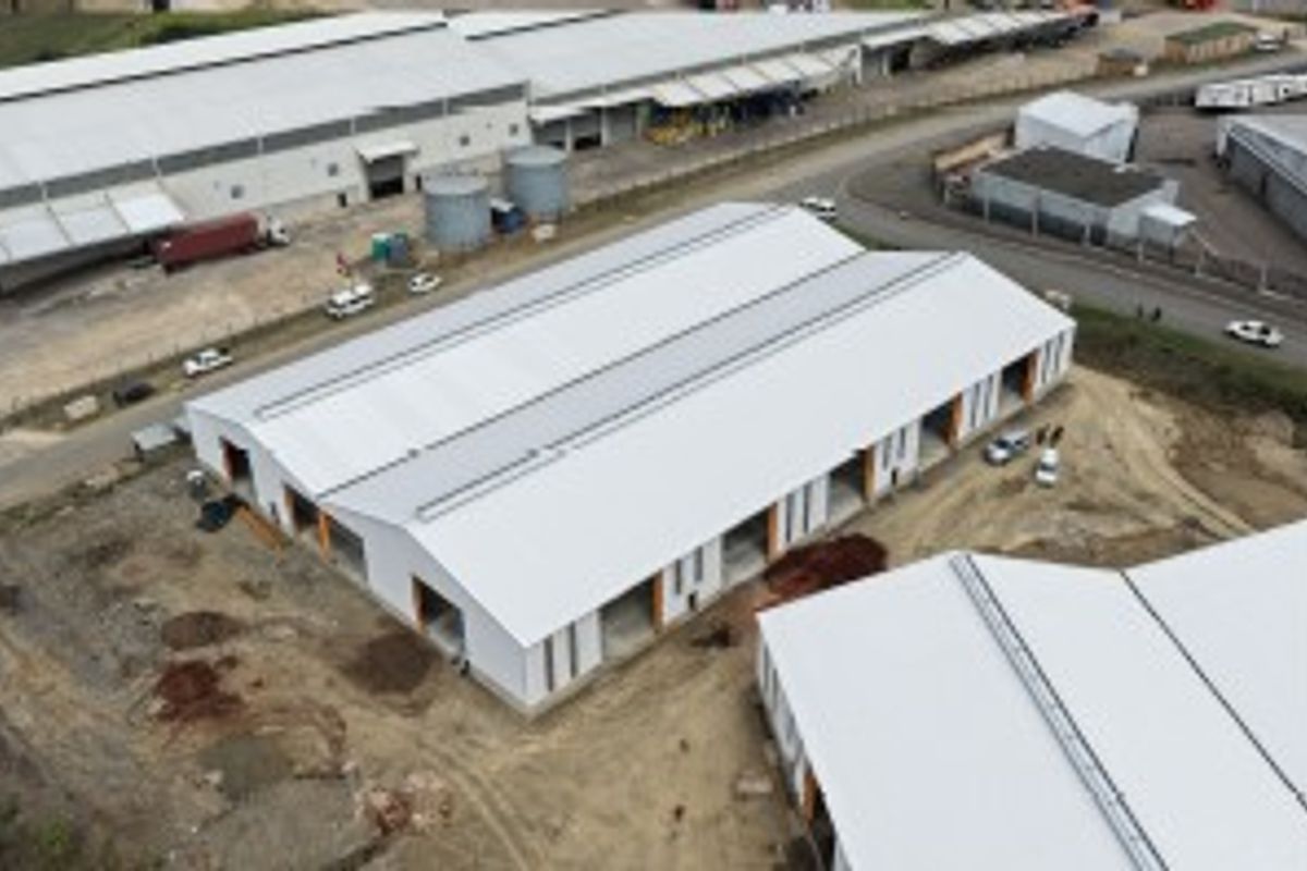 Aerial view of an industrial warehouse complex featuring a large metal roof, multiple roller shutter door openings, and surrounding unpaved yard space.