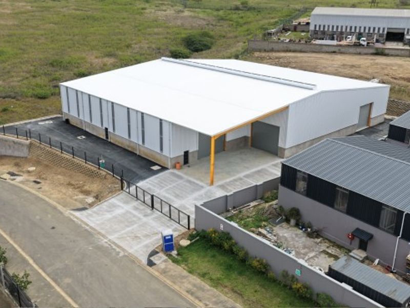 Aerial view of a modern industrial warehouse facility featuring a large metal-clad structure, concrete yard, and secure perimeter fencing.