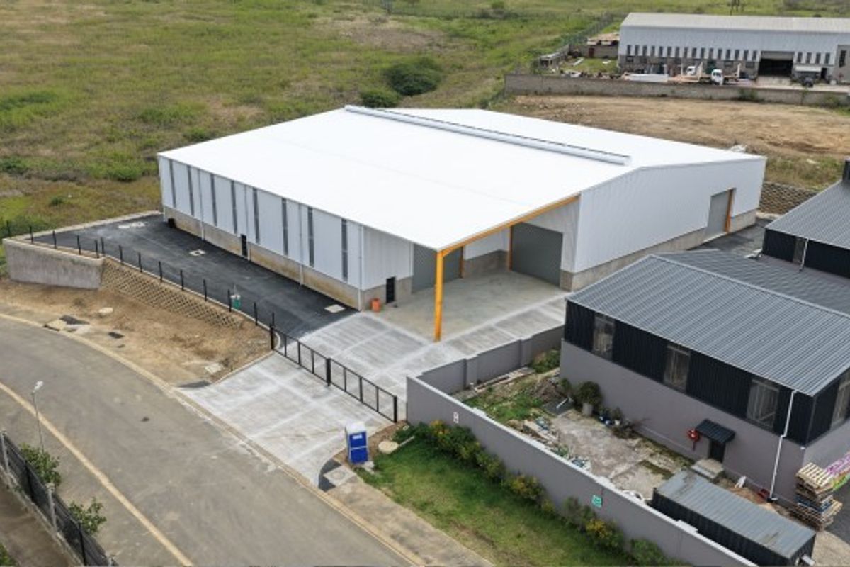 Aerial view of a modern industrial warehouse facility featuring a large metal-clad structure, concrete yard, and secure perimeter fencing.