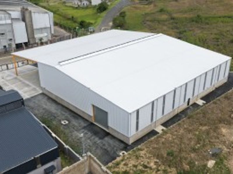 Aerial view of a modern industrial warehouse featuring a large metal-clad structure, pitched roof with skylight, and concrete foundation.