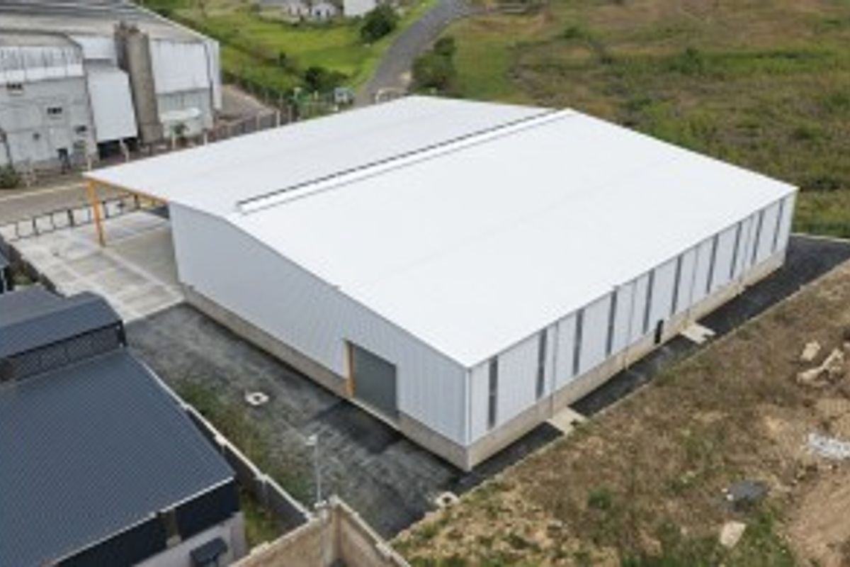 Aerial view of a modern industrial warehouse featuring a large metal-clad structure, pitched roof with skylight, and concrete foundation.