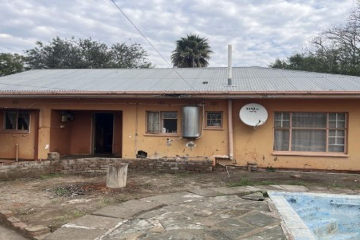 Rear view of the property featuring a corrugated metal roof, swimming pool, and stone patio area requiring maintenance and exterior refurbishment.