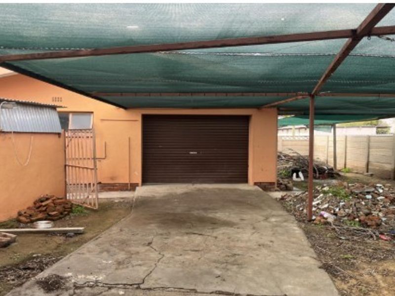 A detached garage featuring a roller shutter door, covered by a large shade cloth carport structure over a cracked concrete driveway.
