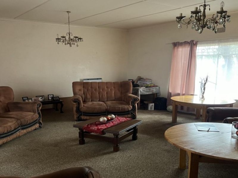 Spacious living room featuring carpet flooring, large windows for natural light, and traditional ceiling light fixtures, offering a blank canvas for modernization.