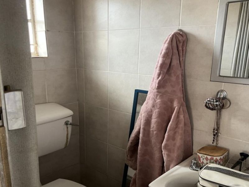 A compact bathroom featuring neutral ceramic wall tiles, a standard toilet, and a wall-mounted washbasin with an integrated mirror.