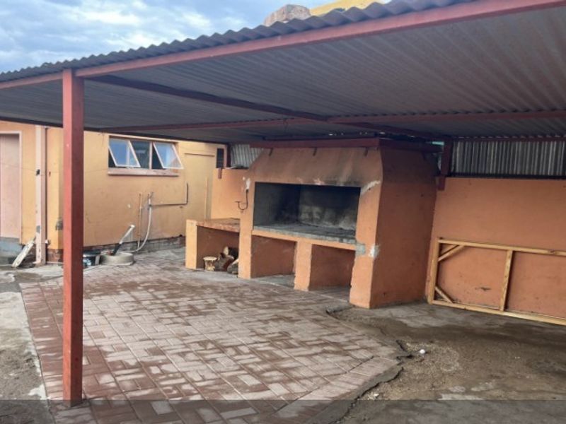 Covered outdoor patio area featuring a built-in braai, paved flooring, and a corrugated iron roof structure.