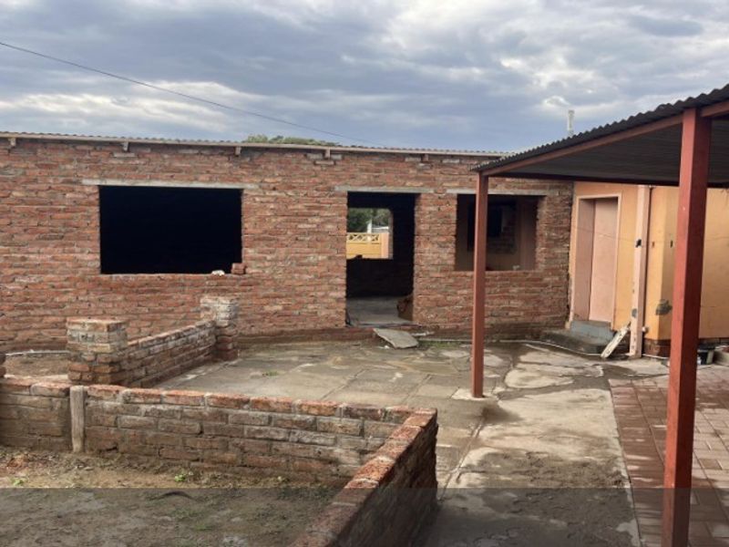 Rear exterior view of a property under construction, featuring exposed brick walls, paved patio area, and a covered carport structure.