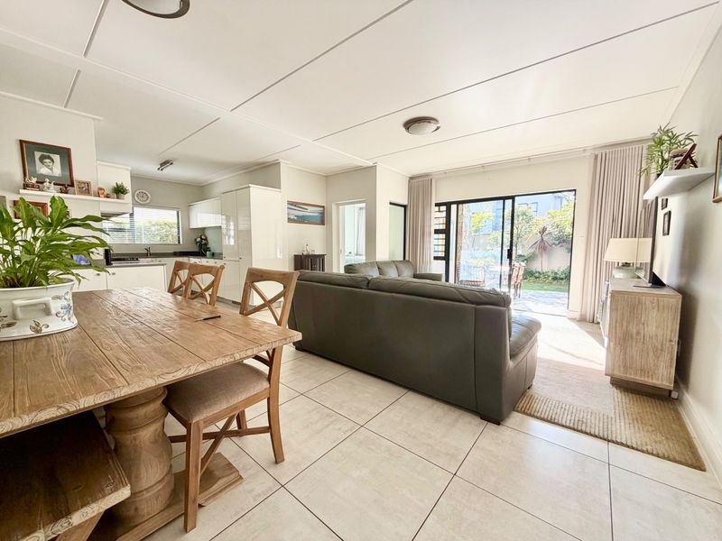Spacious open-plan living and dining area featuring tiled floors, modern kitchen cabinetry, and large sliding doors leading to a private garden.