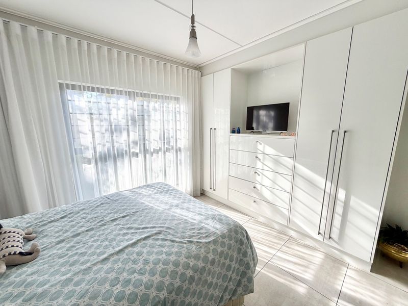 A bright bedroom featuring modern built-in cupboards, tiled flooring, and a large sliding glass door with sheer curtains allowing ample natural light.