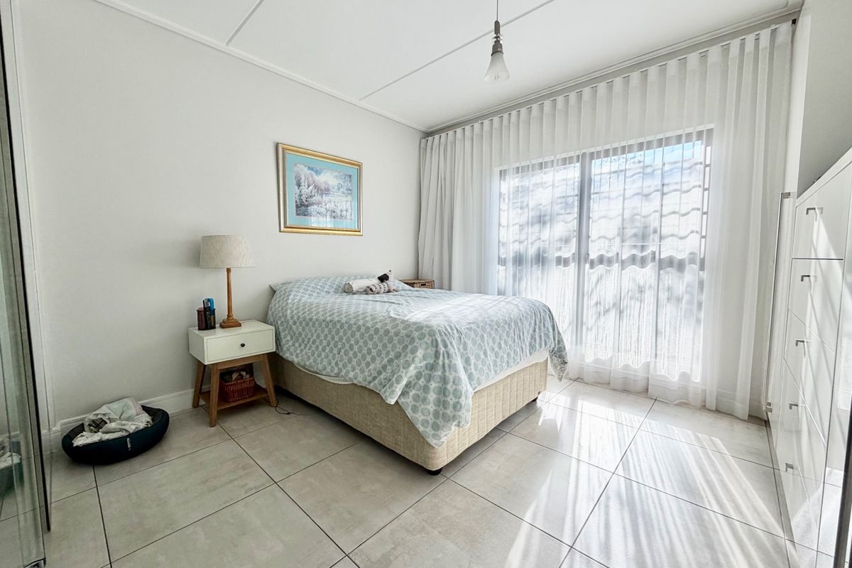 A bright and well-maintained bedroom featuring large format floor tiles, a built-in wardrobe, and a sliding glass door with sheer curtains.