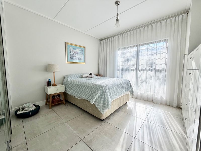 A bright and well-maintained bedroom featuring large format floor tiles, a built-in wardrobe, and a sliding glass door with sheer curtains.