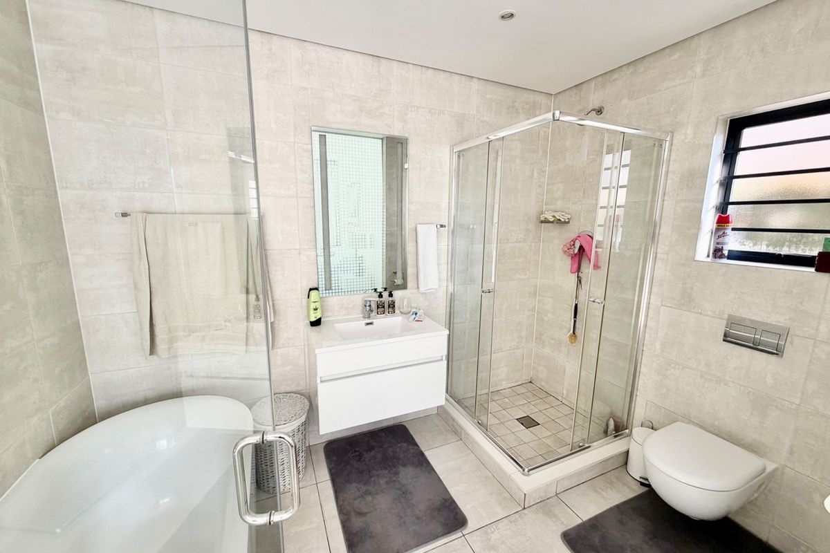 Modern bathroom featuring a freestanding bathtub, glass-enclosed shower, wall-mounted vanity, and wall-hung toilet with neutral floor-to-ceiling tiling.
