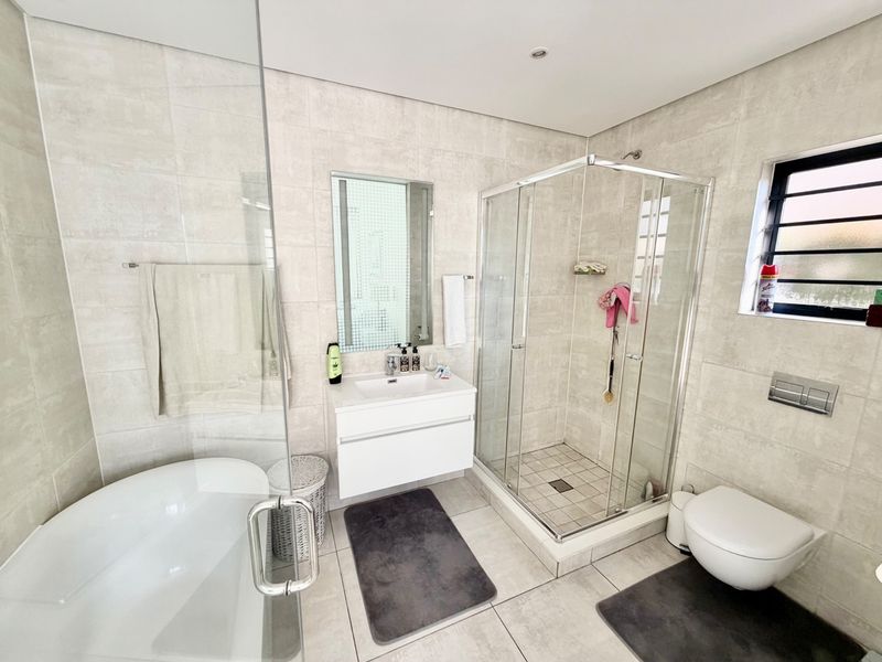 Modern bathroom featuring a freestanding bathtub, glass-enclosed shower, wall-mounted vanity, and wall-hung toilet with neutral floor-to-ceiling tiling.