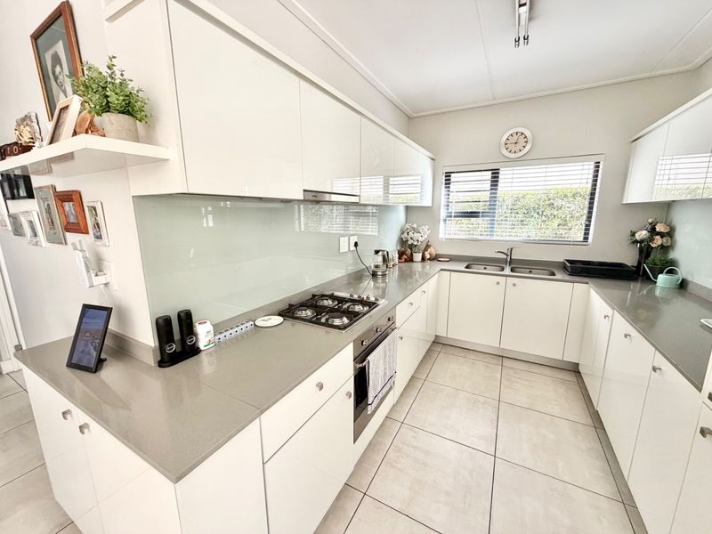 Modern kitchen featuring white high-gloss cabinetry, stone countertops, a gas hob, built-in oven, and a sleek glass splashback with tiled flooring.