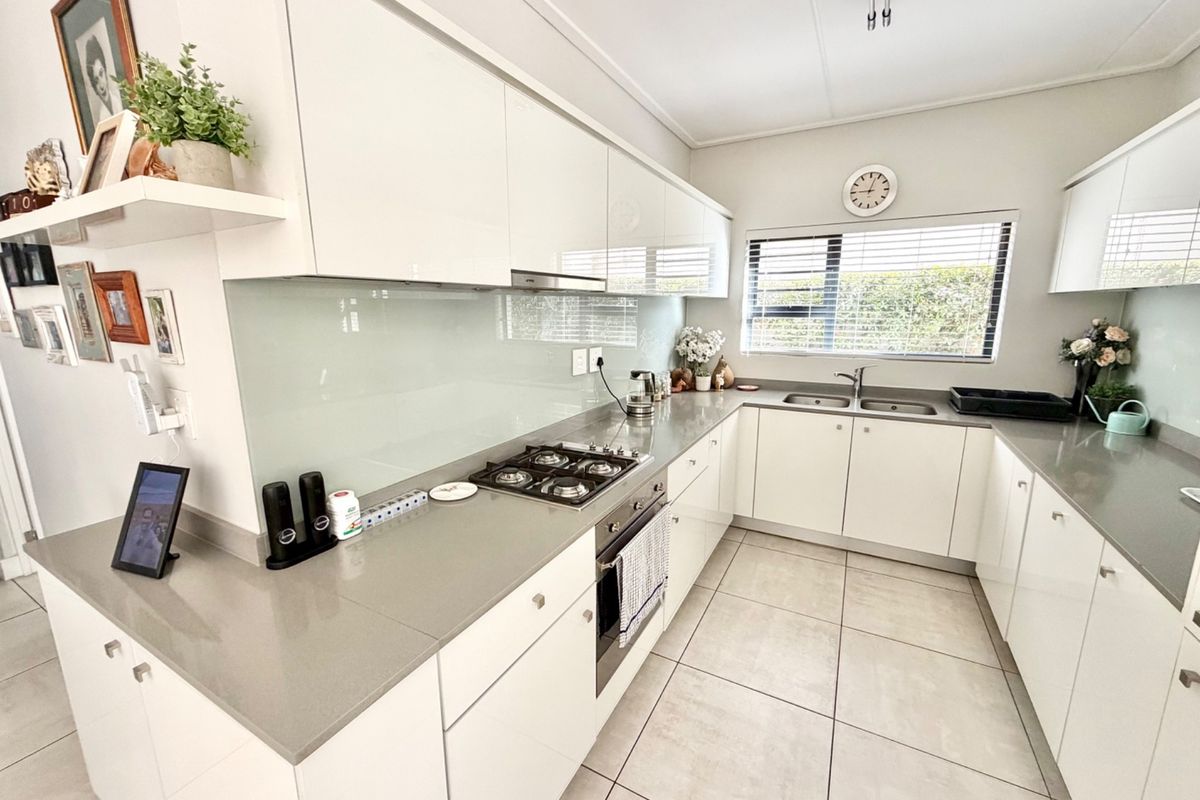 Modern kitchen featuring white high-gloss cabinetry, stone countertops, a gas hob, built-in oven, and a sleek glass splashback with tiled flooring.
