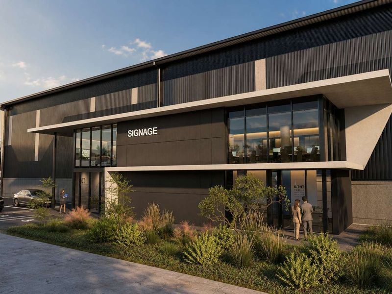 Modern industrial building facade featuring dark metal cladding, expansive glass windows, and a sleek concrete canopy entrance with dedicated parking.