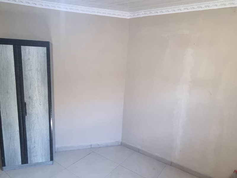 A simple, empty bedroom featuring tiled flooring and decorative ceiling cornicing, requiring cosmetic updates to the wall finishes.