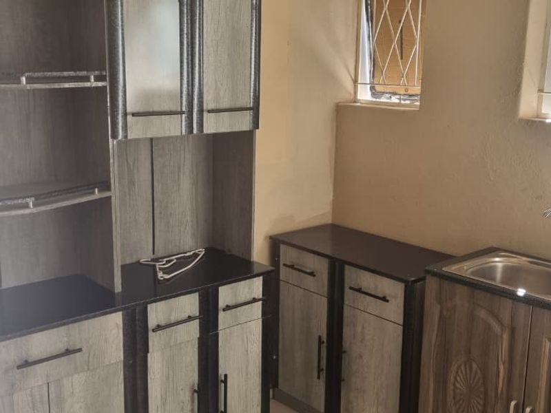 A functional kitchen area featuring built-in cabinetry, a double bowl sink with mixer tap, and security bars on the windows.