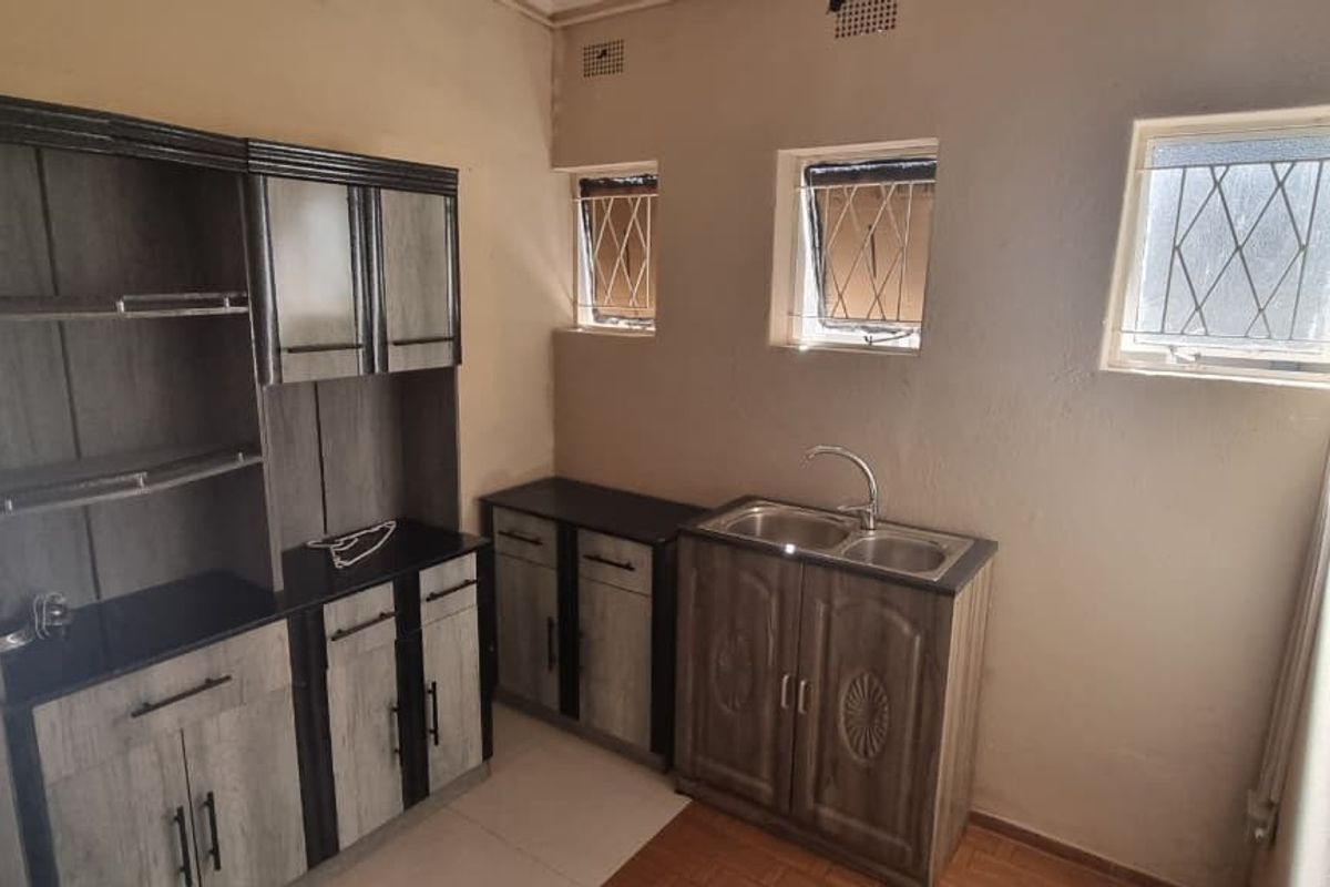 A functional kitchen area featuring built-in cabinetry, a double sink, and tiled flooring with security-barred windows providing natural light.