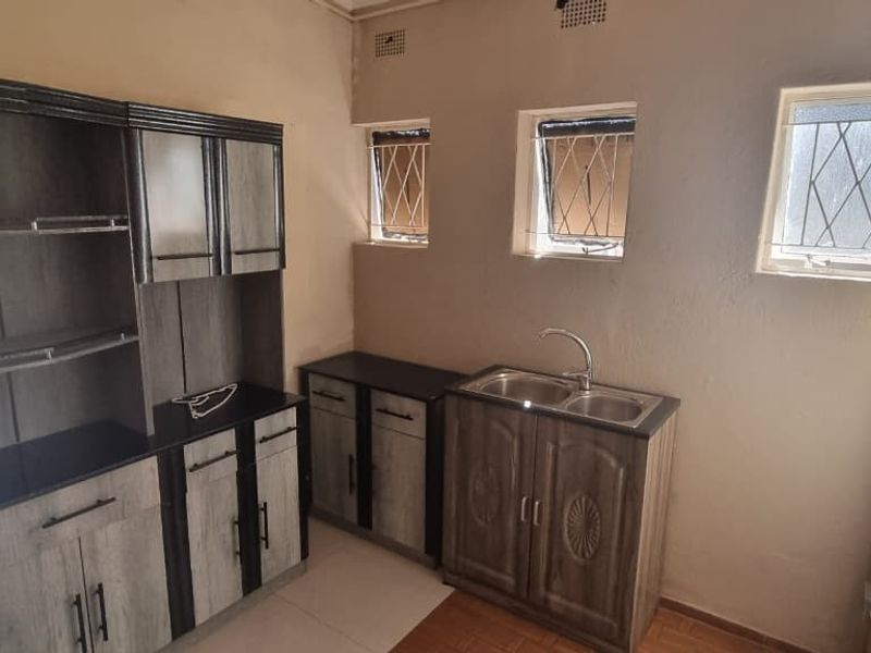 A functional kitchen area featuring built-in cabinetry, a double sink, and tiled flooring with security-barred windows providing natural light.