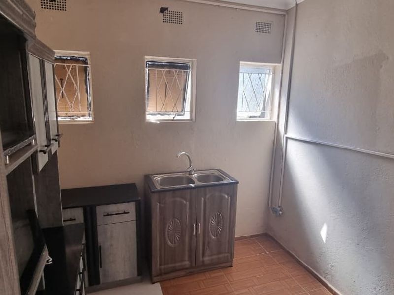 A functional laundry area featuring a stainless steel sink, built-in cabinetry, tiled flooring, and security-fitted windows.