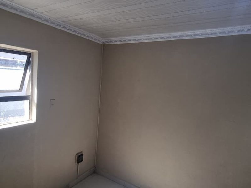 An empty bedroom featuring a top-hung window, decorative ceiling cornice, and textured ceiling panels, requiring minor cosmetic updates to the wall finishes.