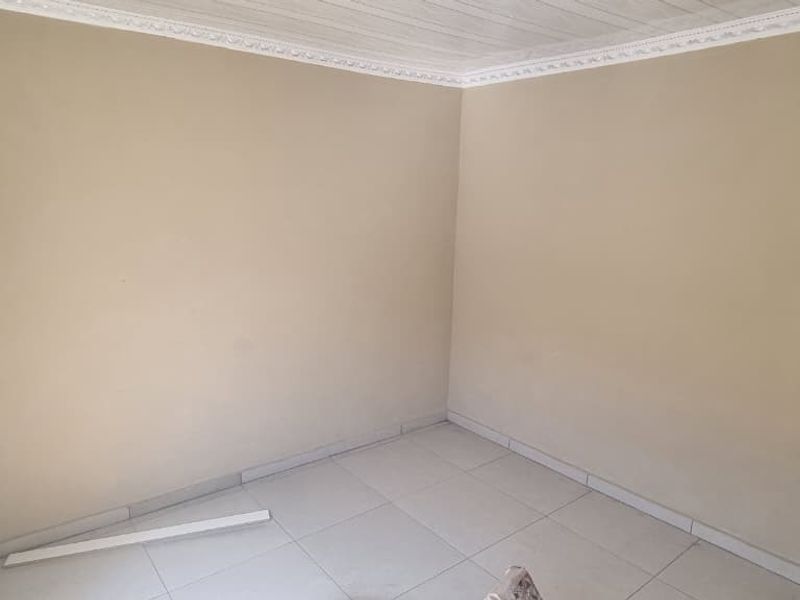 An empty bedroom featuring tiled flooring, ceiling cornice, and neutral wall paint, requiring minor finishing touches to the baseboards and electrical fixtures.