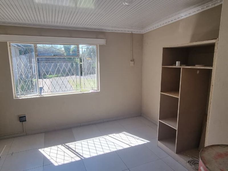 A vacant bedroom featuring tiled flooring, a panelled ceiling, and a built-in shelving unit, with security bars installed on the window.