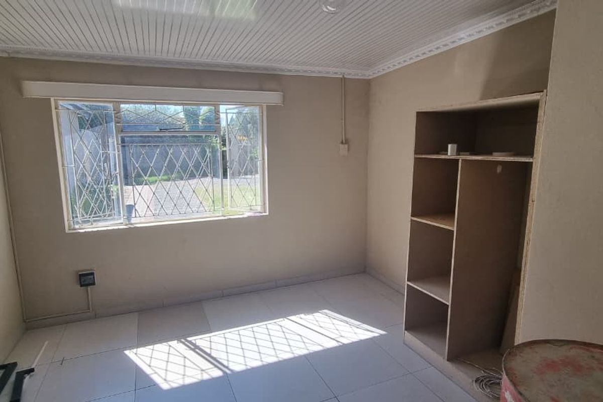 A vacant bedroom featuring tiled flooring, a panelled ceiling, and a built-in shelving unit, with security bars installed on the window.