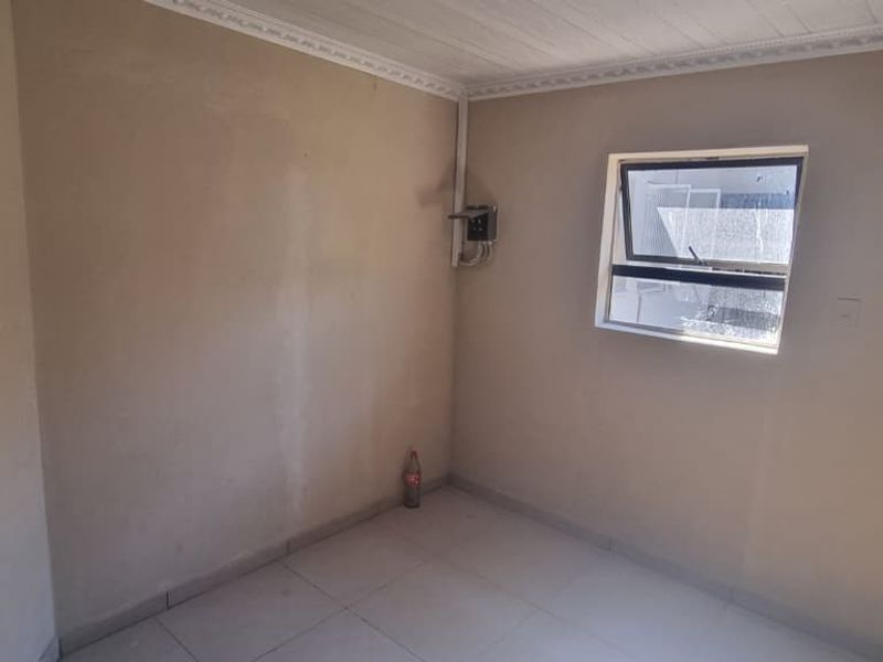 A compact, empty bedroom featuring tiled flooring, a top-hung window, and exposed electrical infrastructure, offering a blank canvas for renovation.